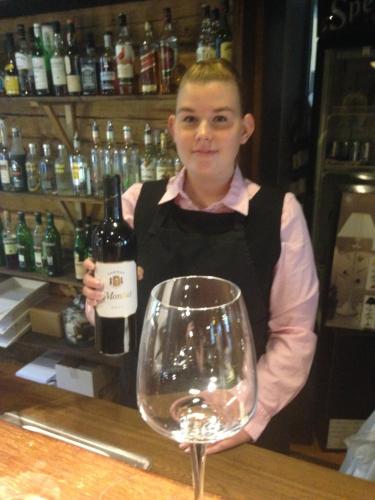 a woman standing behind a bar with a wine glass at Hotell Plevnagården in Malmköping