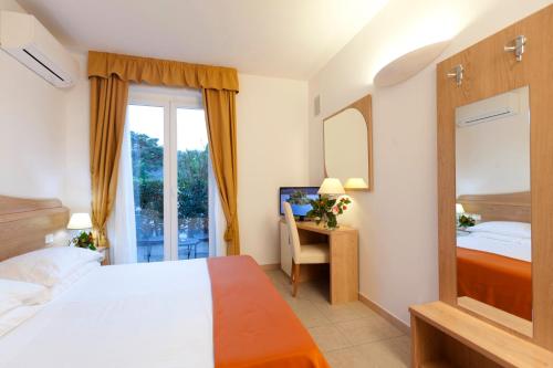 a bedroom with a bed and a desk with a mirror at Hotel Villa Smeraldo in Orbetello