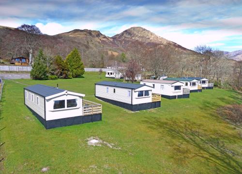 a row of houses in a field with mountains in the background at Appin Holiday Homes -Caravans, Lodges, Shepherds Hut and Train Carriage stays in Appin