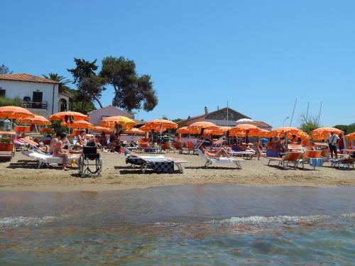 a beach with orange umbrellas and people on the sand at Hotel Villa Smeraldo in Orbetello