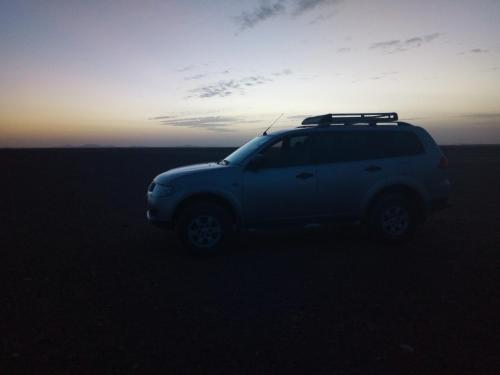 a white suv parked in the desert at sunset at Sahara Desert Camp in Hassilabied