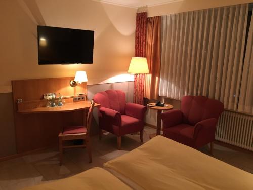 ein Hotelzimmer mit roten Stühlen, einem Schreibtisch und einem Bett in der Unterkunft Altes Gasthaus Kuhr - Hotel & Restaurant in Papenburg