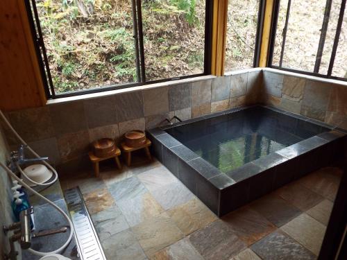 a large tub in a bathroom with windows at Kurasako Onsen Sakura in Minamioguni