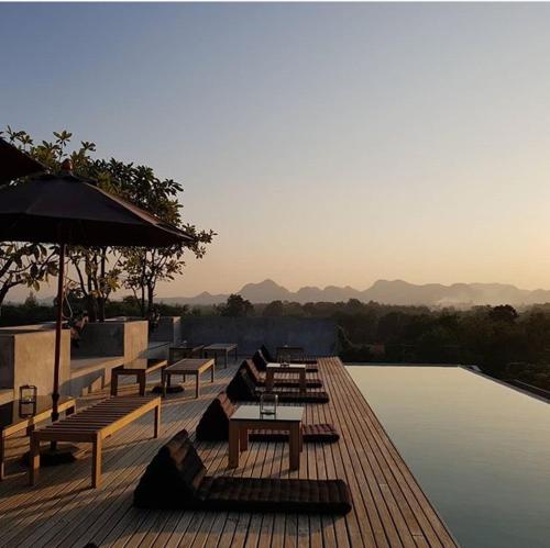 a deck with benches and an umbrella next to a pool at Inchantreedoopool in Kanchanaburi