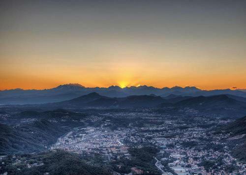 a view of a city with the sun setting behind mountains at Bellavista Boutique Hotel in Brunate