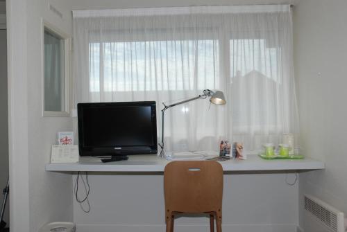 a desk with a monitor and a lamp and a chair at Campanile Creil - Villers-Saint-Paul in Villers-Saint-Paul