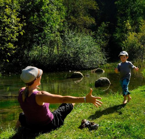 a woman and a child playing in the grass near a river at Active Hotel Monte Giner in Mezzana