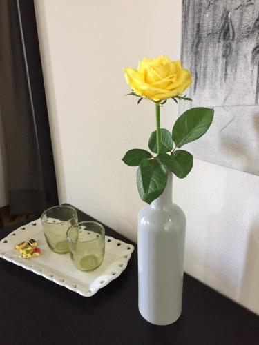 a yellow rose in a white vase next to two glasses at B&B Martina in Assemini