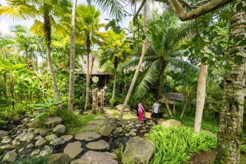 two people walking through a garden with palm trees at Adiwana Dara Ayu Villas in Payangan