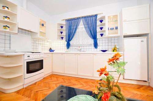 una cocina con armarios blancos y cortinas azules en Apartmani Ivana & Toni, en Gradac