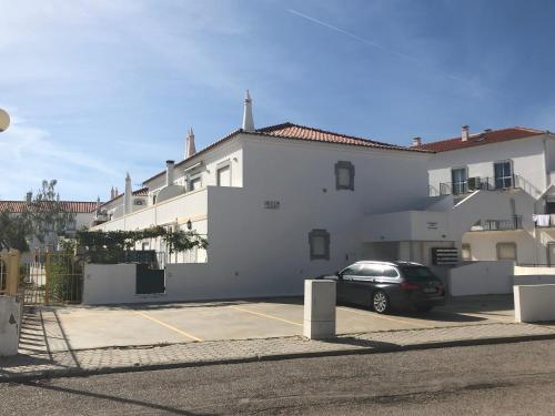 a white building with a car parked in a parking lot at Altura da Maré - Apartamento Duna in Altura