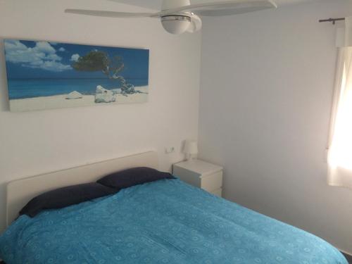 sypialnia z niebieskim łóżkiem i obrazem na ścianie w obiekcie HELLO OLIVA BEACH Bungalow Bajo w mieście Oliva