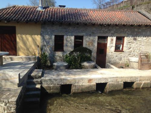a stone house with a pond in front of it at Moinho das Cavadas in Ponte da Barca