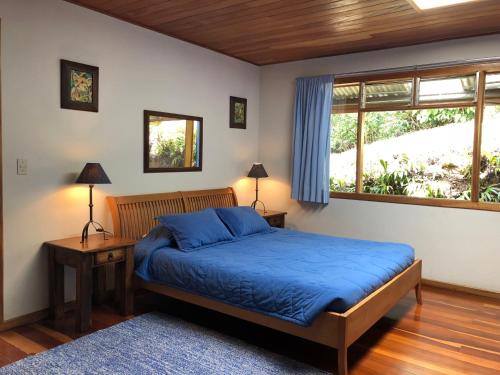 a bedroom with a bed with blue sheets and a window at Casa Cañitas in Monteverde Costa Rica