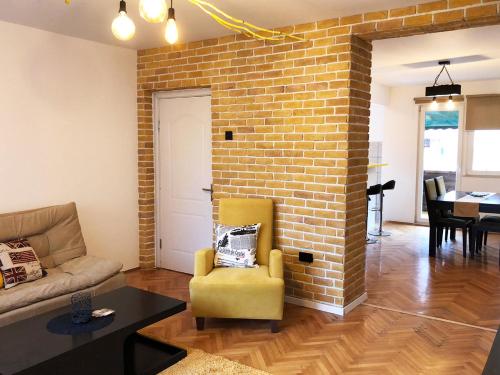 - un salon avec un mur en briques et une chaise jaune dans l'établissement Lemon Tree Apartment, à Pristina