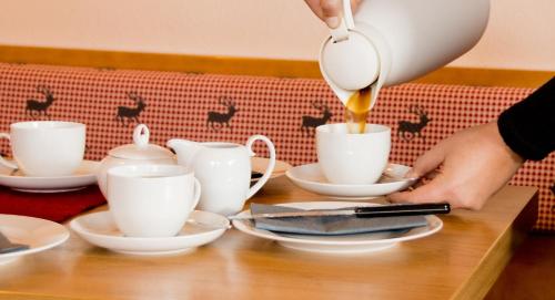 een persoon die koffie in witte bekers giet op een tafel bij Pension Schuasterhof in Bodenmais