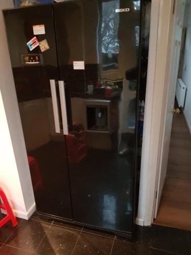 a black refrigerator in a hallway with stickers on it at Rooms in a Family Home in London