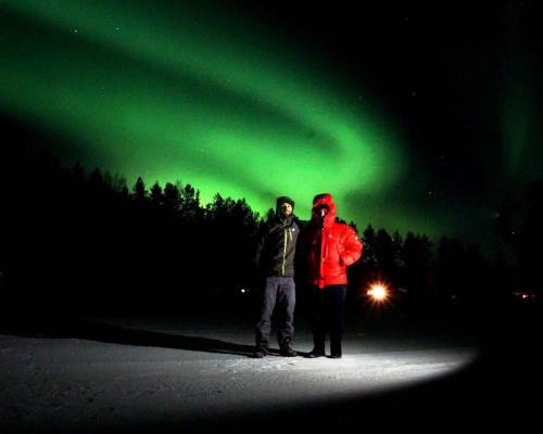 dos personas de pie bajo la verde aurora boreal en Palojärven Lomakeskus en Sonka