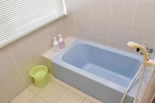 a bathroom with a blue tub and a green trash can at Cottage Sachi in Nakijin