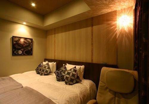a bedroom with a bed with pillows and a chair at Hotel Coco Grand in Takasaki
