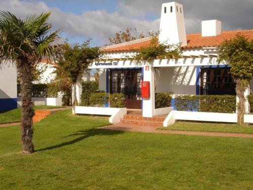 a white house with a palm tree in the yard at Parque Campismo Porto Côvo in Porto Covo