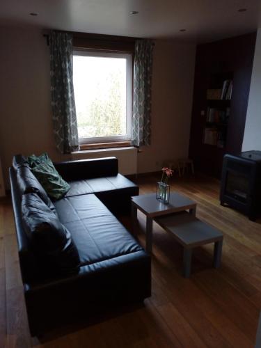 a living room with a black leather couch and a window at La petite maison in Aywaille