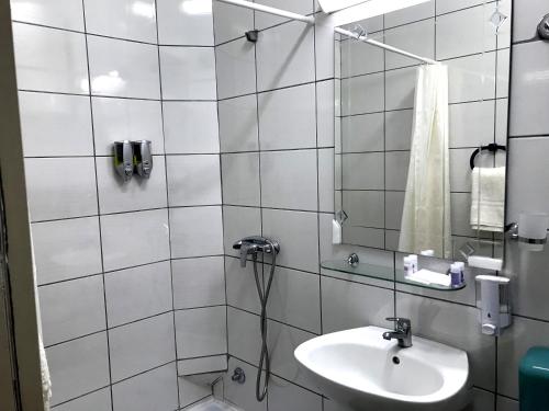 La salle de bains est pourvue de carrelage blanc, d'un lavabo et d'une douche. dans l'établissement Kingdom Rooms Visoko, à Visoko