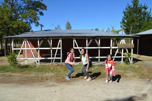 a woman and two girls standing in front of a barn at Coyunche Cabañas y Camping Laja & San Rosendo in Laja