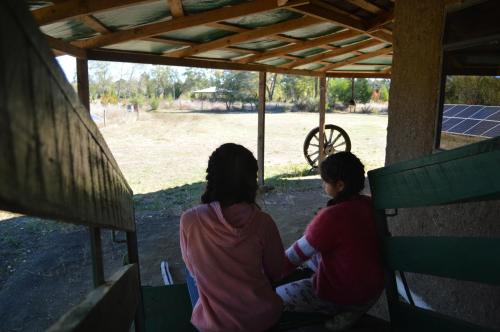 two women sitting on a bench under a roof at Coyunche Cabañas y Camping Laja & San Rosendo in Laja