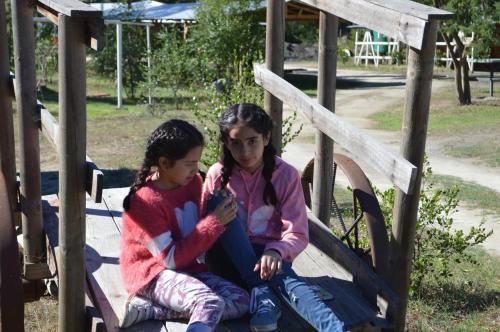 two young girls sitting on a slide at a playground at Coyunche Cabañas y Camping Laja & San Rosendo in Laja
