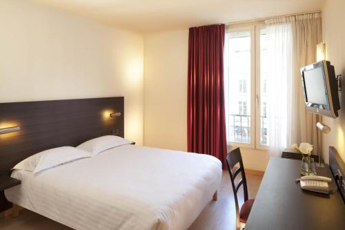 a hotel room with a bed and a desk and a tv at Hôtel Oceania Brest in Brest