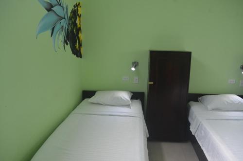 two beds in a room with white sheets and a plant at Room2Board Hostel and Surf School in Jacó