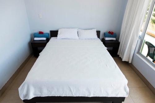 a bedroom with a bed with white sheets and a window at Room2Board Hostel and Surf School in Jacó