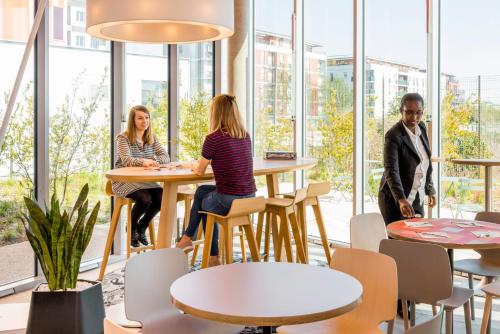 a group of people sitting at tables in a room with windows at Aparthotel Adagio Access Paris Massy Gare in Massy