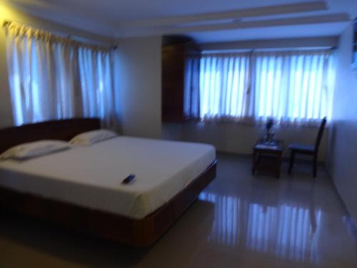 a bedroom with a bed and a chair and windows at Hotel Susee Park in Tiruchchirāppalli