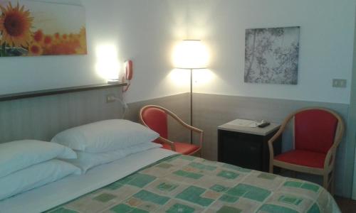 リミニにあるHotel Arosのベッド1台、椅子2脚、ランプが備わる客室です。