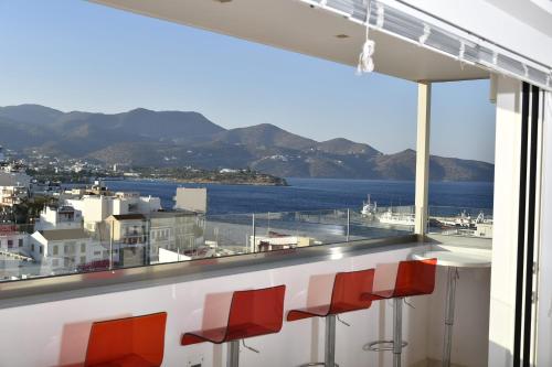 a bar with red chairs and a view of the water at Ikaros Art Hotel in Agios Nikolaos