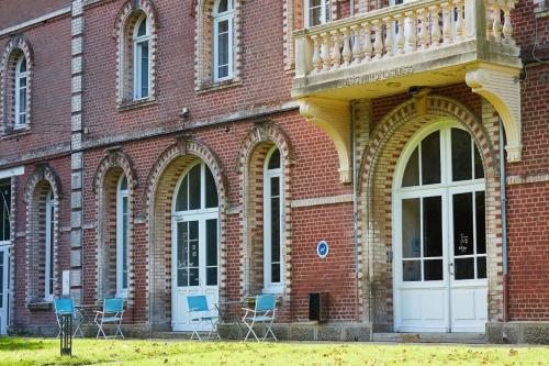 a red brick building with chairs and a balcony at The Originals Hôtel Le Cise Restaurant Chambres et Suites in Ault
