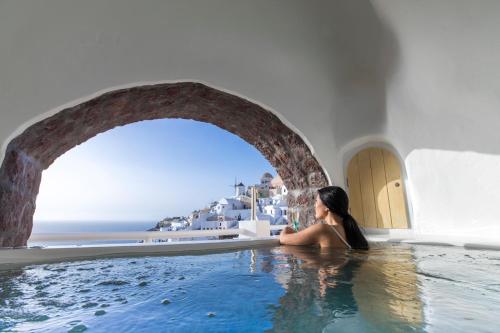 a woman sitting in a hot tub with a view of the ocean at Art Maisons Oia Castle in Oia