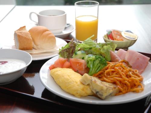 una mesa con un plato de comida y un vaso de zumo de naranja en J Hotel Rinku en Tokoname