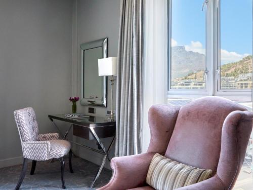 a living room with a pink chair and a desk with a mirror at Queen Victoria Hotel by NEWMARK in Cape Town