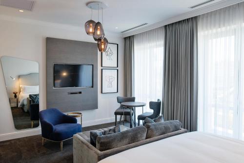 a hotel room with a bed and a couch and a tv at The Manor House at the Queen Victoria Hotel by NEWMARK in Cape Town