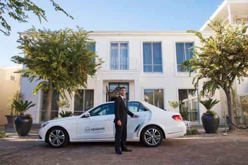 a man in a suit standing next to a white car at The Manor House at the Queen Victoria Hotel by NEWMARK in Cape Town
