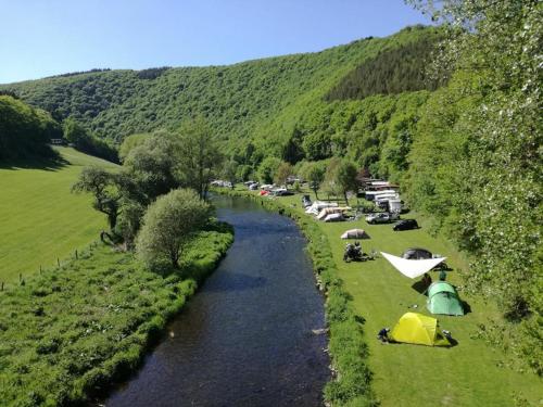 a river with tents on the grass next to a mountain at LeafMaxi - Camping du Nord in Bourscheid