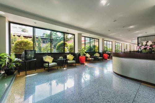 a lobby with chairs and tables and windows at Capital Mansion - SHA Certified in Bangkok