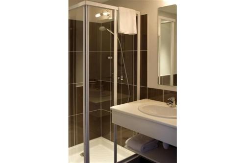 La salle de bains est pourvue d'un lavabo et d'une douche en verre. dans l'établissement Hôtel Majestic, à Lourdes