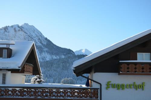 a building with snow on the roof with mountains in the background at Hotel Cafe Fuggerhof in Oberstdorf
