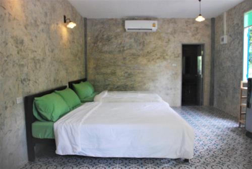 a bedroom with a large white bed with green pillows at Baantantara in Suan Phung