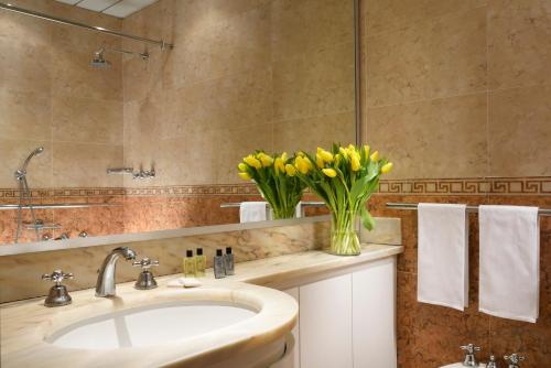 a bathroom with a sink and a vase of yellow flowers at UNA Hotels Hotel & Residence Contessa Jolanda Milano in Milan