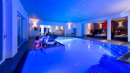 a woman sitting in a swimming pool at night at Thula Wellnesshotel Bayerischer Wald in Lalling